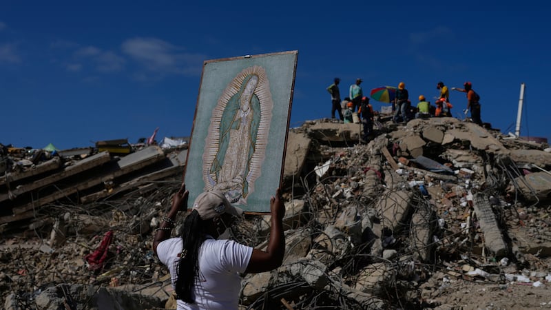 A woman holds a painting of the Virgin Mary as she accompanies a Catholic priest supporting...